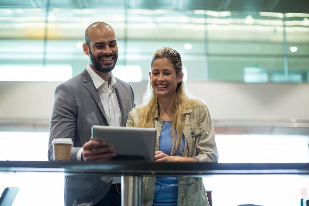 smiling-couple-using-digital-tablet-waiting-area